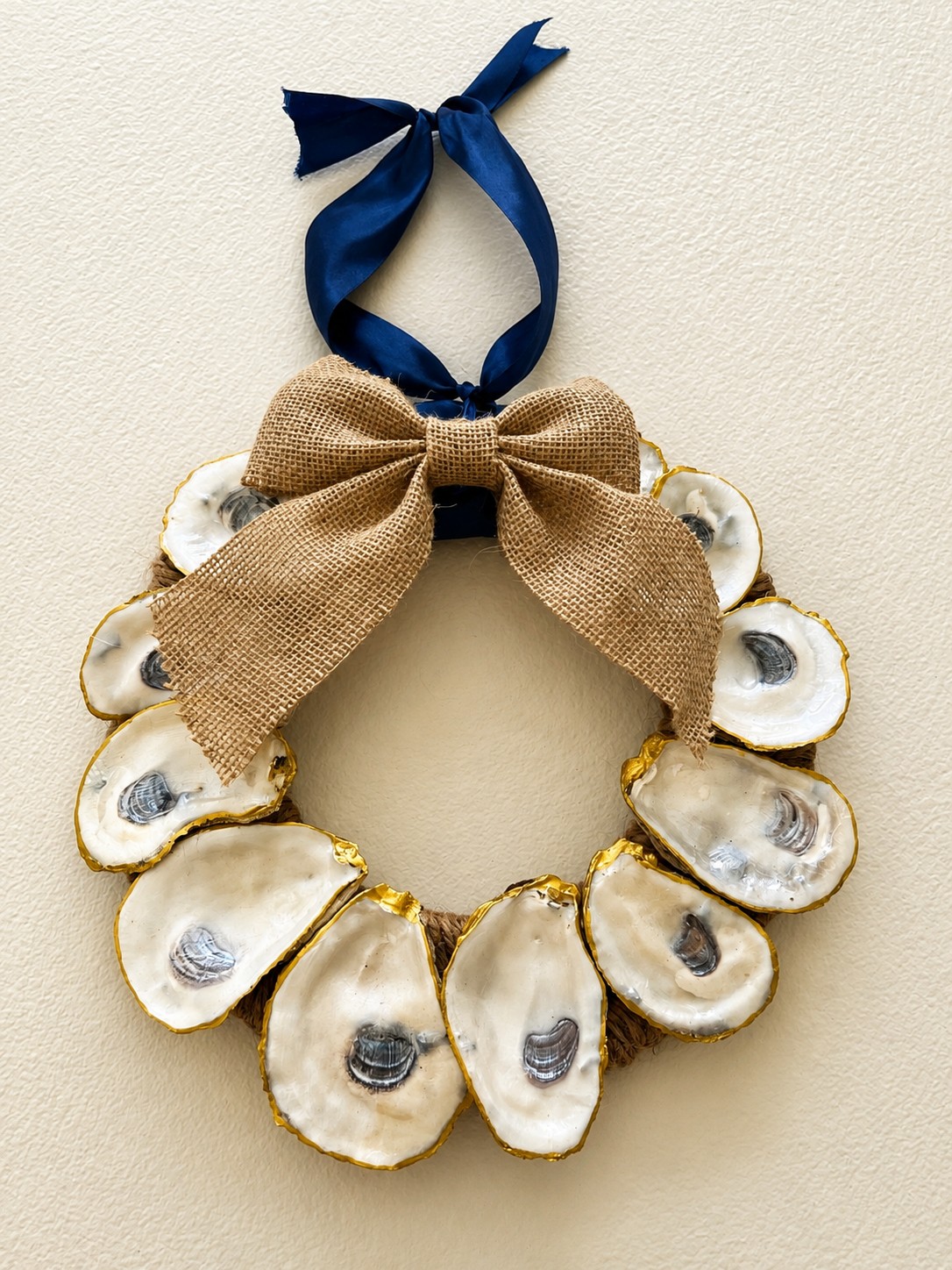 Gold-edged oyster shell wreath with a burlap bow and navy ribbon